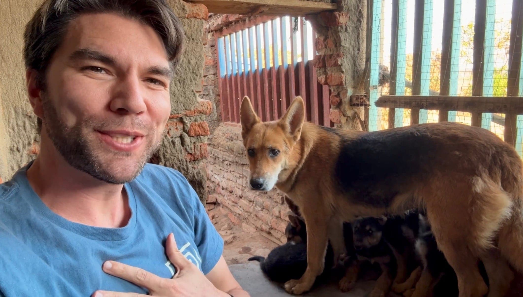 David sits in a dog house beside a German Shepherd mother at the When the Saints safe home.